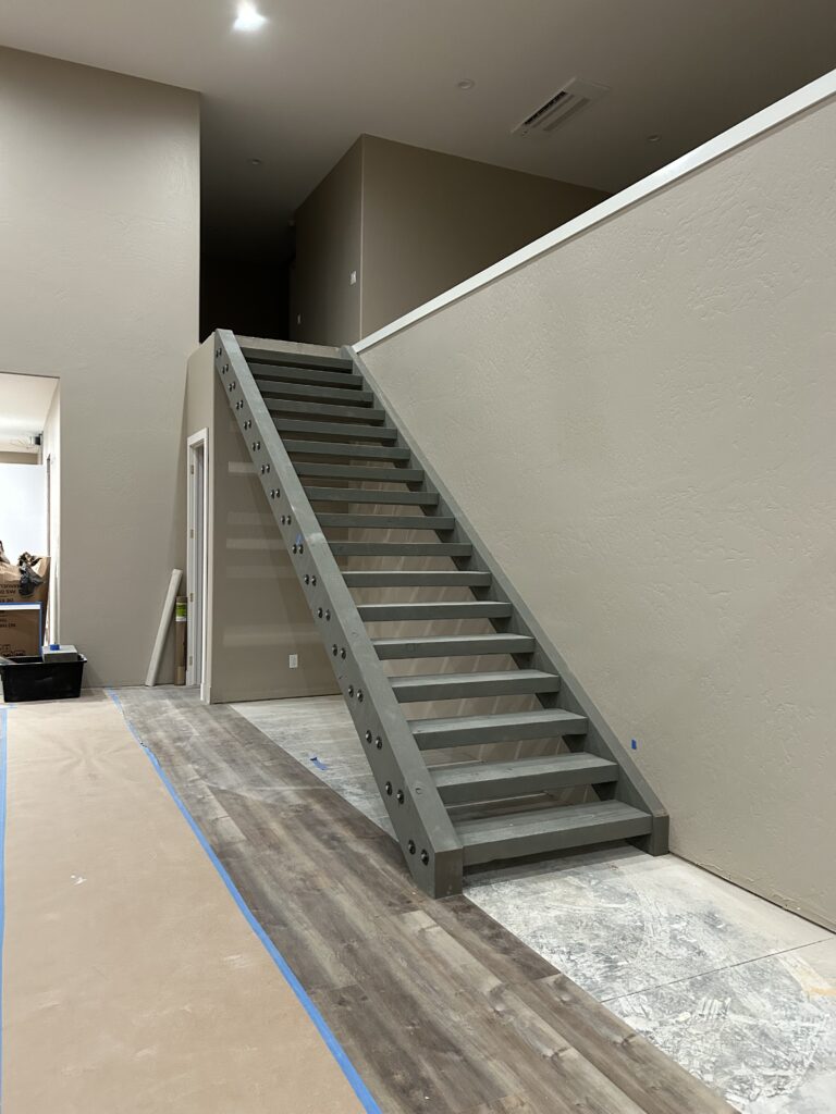 Modern open-tread staircase under construction with exposed steel stringers and unfinished flooring.